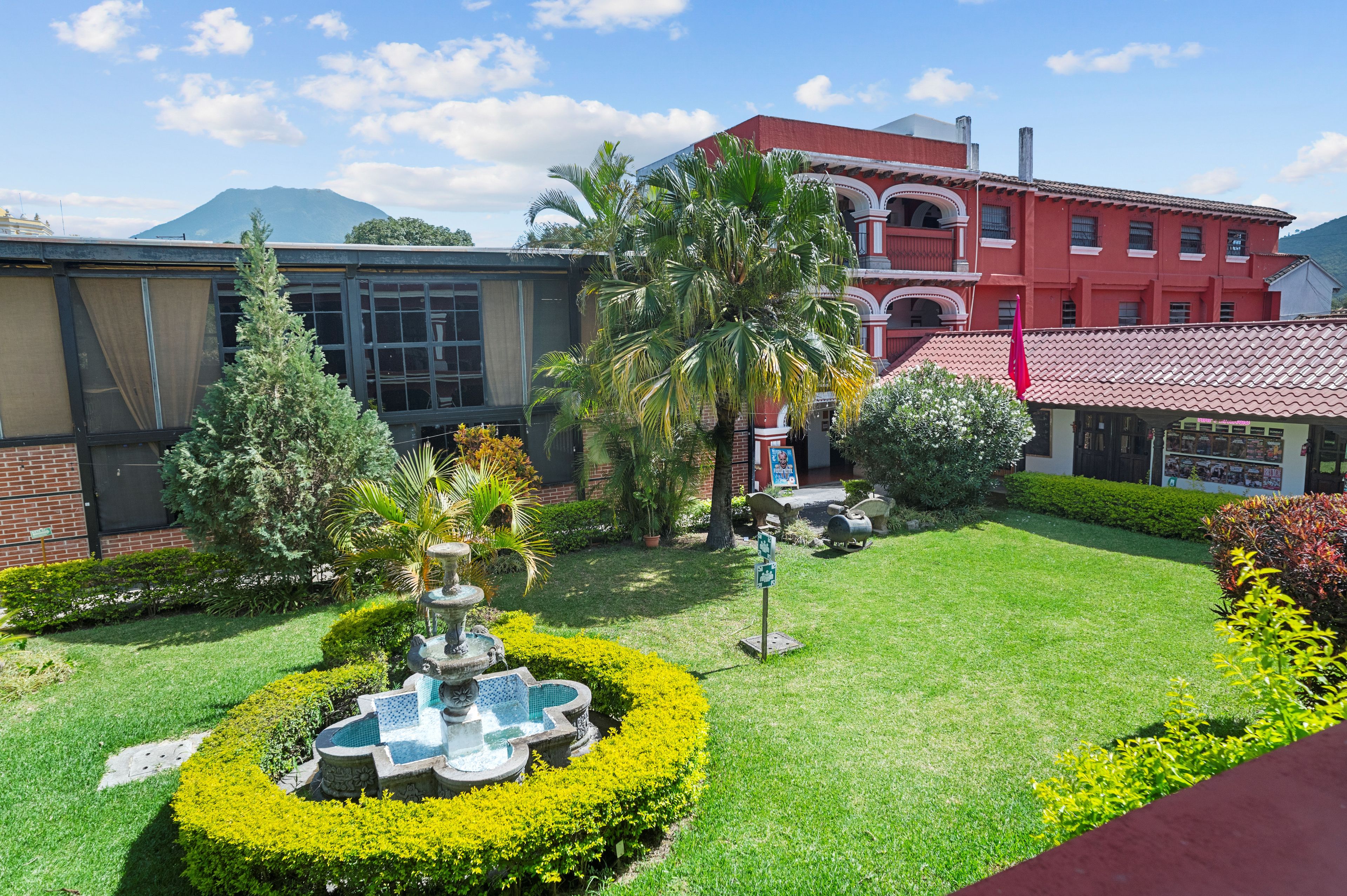 A courtyard with a fountain, manicured lawn, and a red building with balconies.