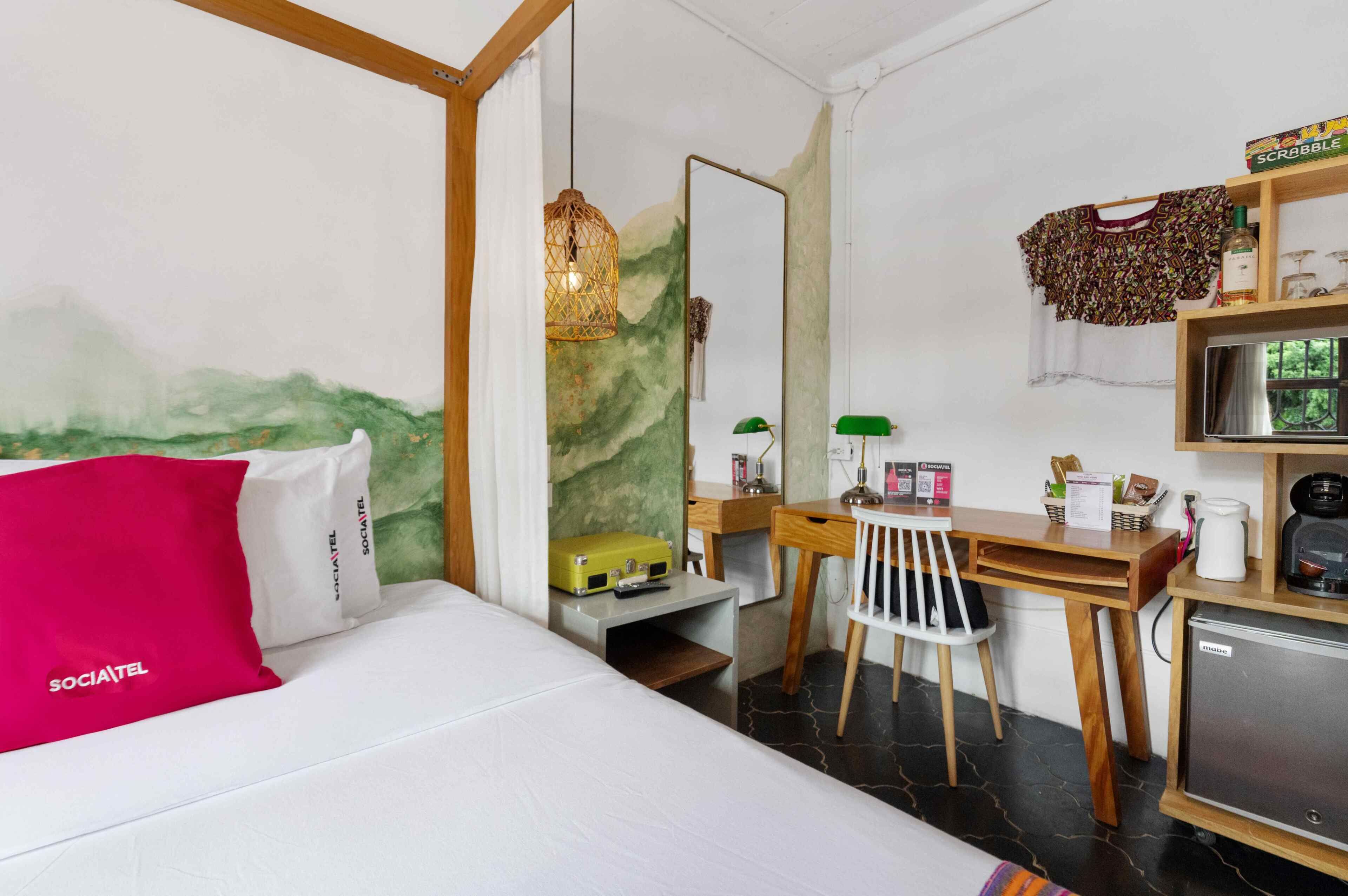 Una habitación de hotel con cama, escritorio, silla y un refrigerador pequeño.