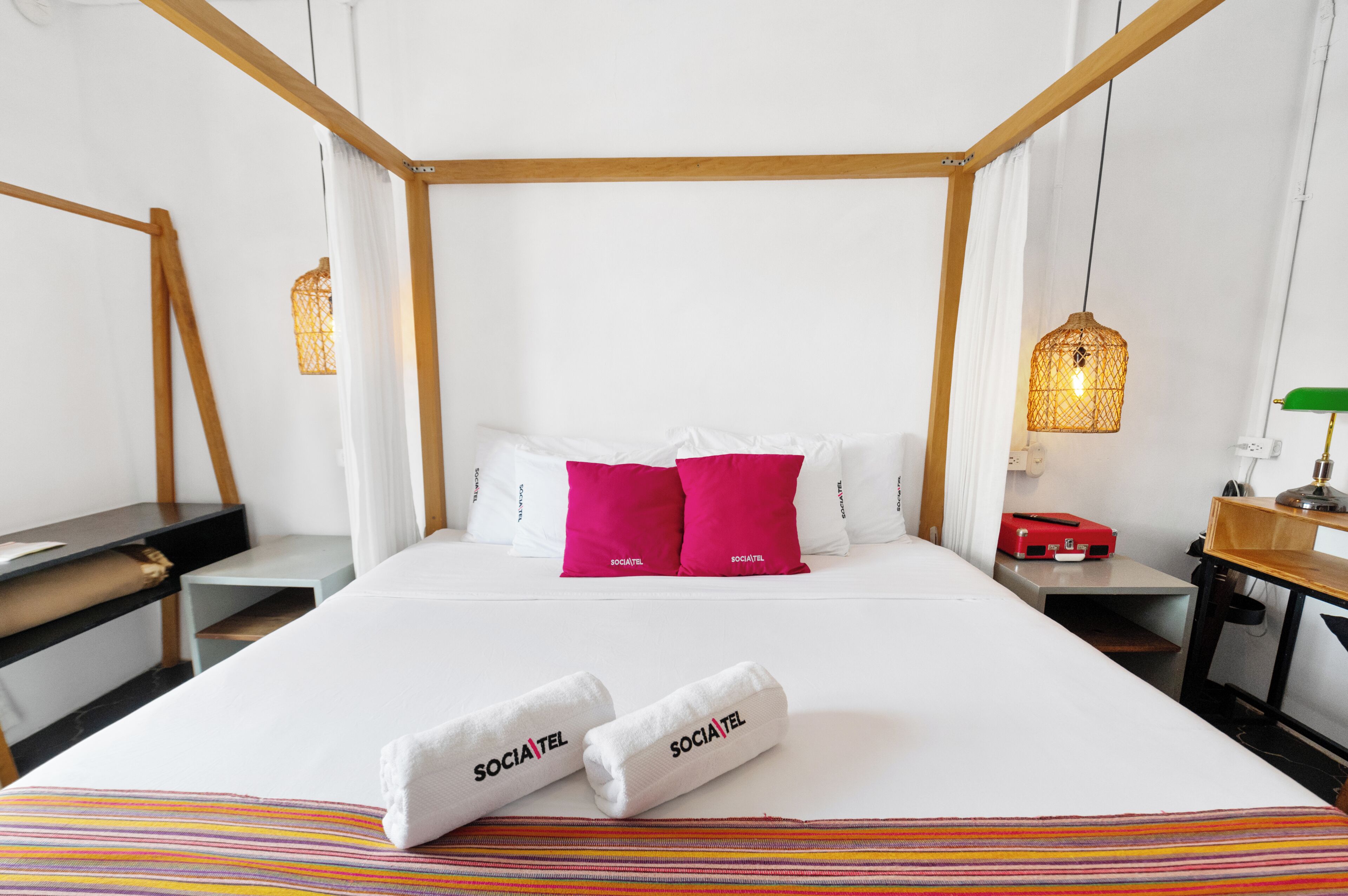 Una habitación de hotel con cama con dosel, un escritorio, una silla, una mesita de noche, una lámpara y un candelabro colgante.
