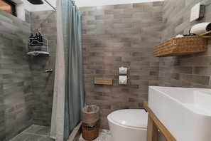 A bathroom with a shower, toilet, and sink. There is a sign on the wall, a basket on the floor, and a towel rack. - Socialtel Antigua (Antigua Guatemala)