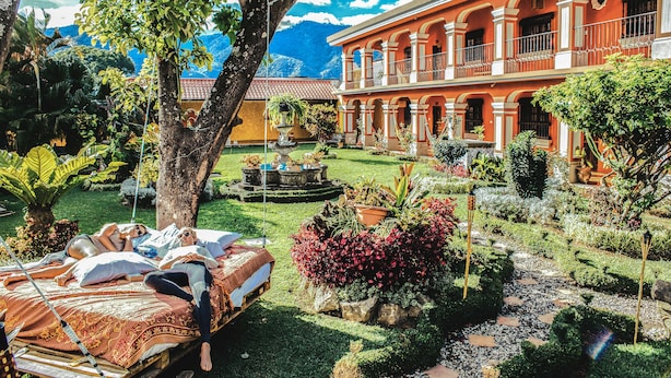 Une cour avec un parterre de fleurs, une fontaine et un bâtiment orné de colonnes.