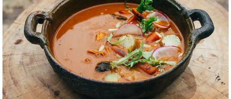 Un tazón rústico de sopa con diferentes verduras y hierbas, sobre una superficie de madera.