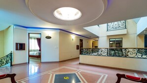 Eine Hotellobby mit einem geometrisch gemusterten Boden, einer zentralen Leuchte und einem Balkon mit aufwendigen Geländern.
