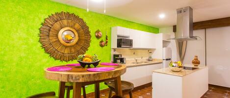 A kitchen with a green wall, a round wooden table with chairs, a microwave, and a stove.