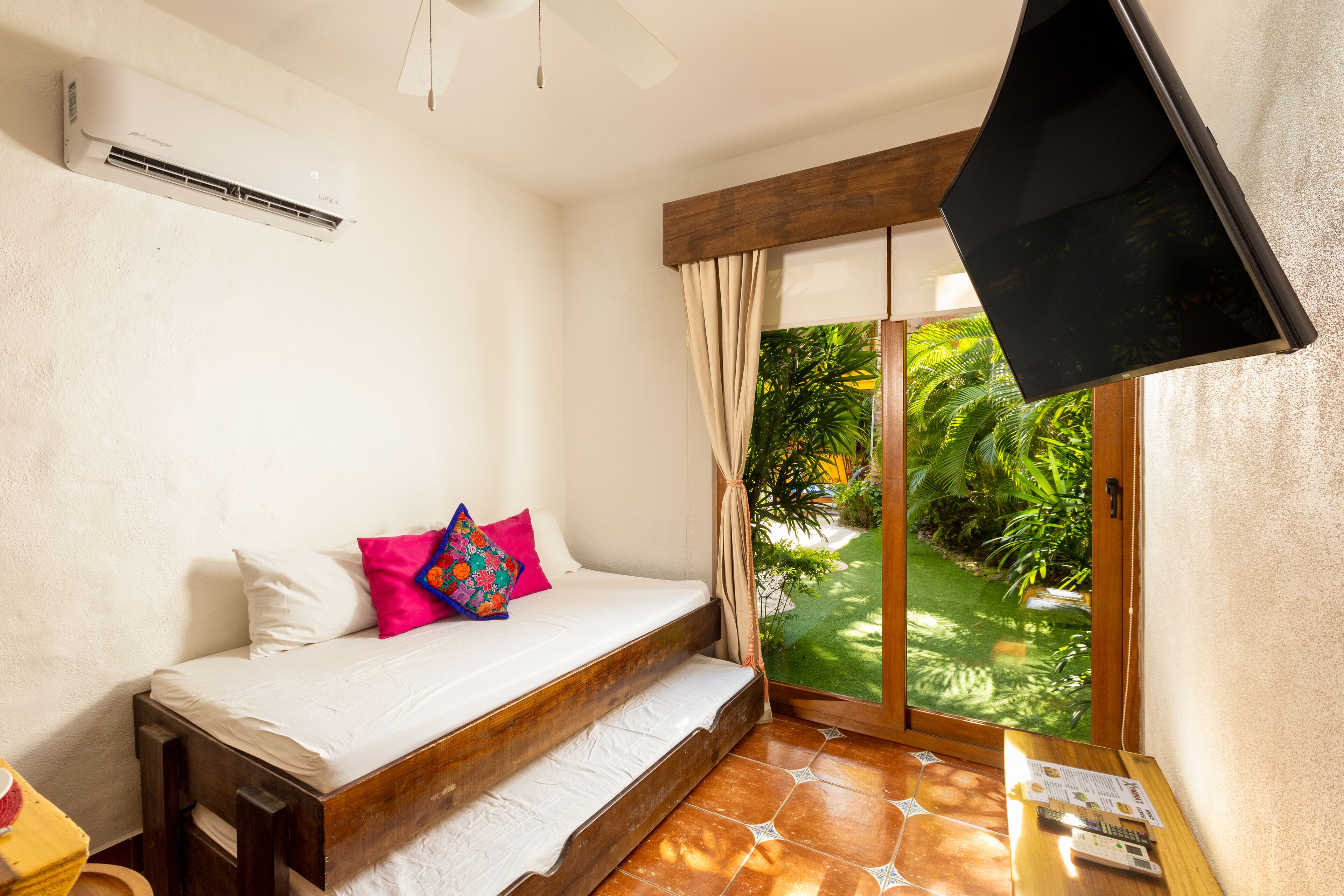 A bedroom with a bed, a TV, a window with curtains, and a view of greenery outside.