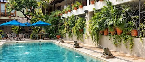 Una piscina con agua azul cristalina, rodeada por un edificio con balcones decorados con plantas en macetas.