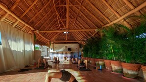 Un estudio de yoga con techo de paja, vigas de madera y plantas en macetas.