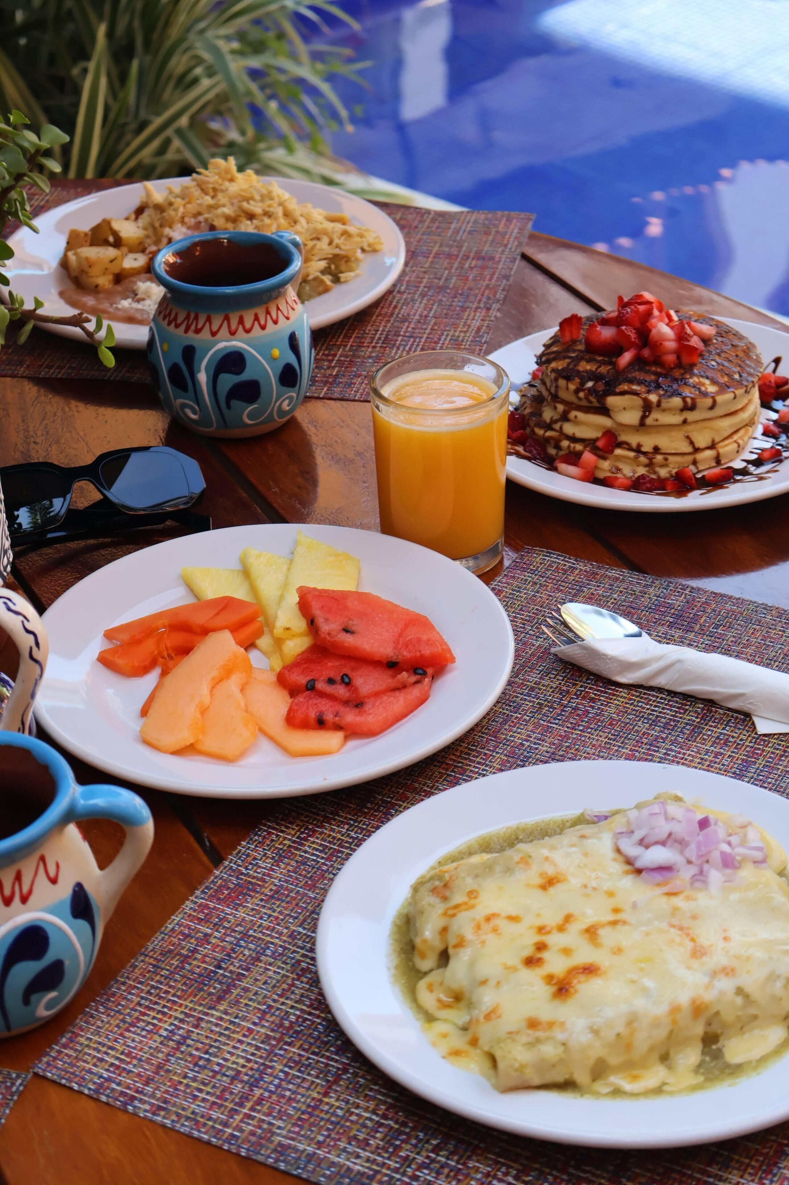 Una mesa con alimentos para el desayuno, como fruta, tortitas y una bebida.