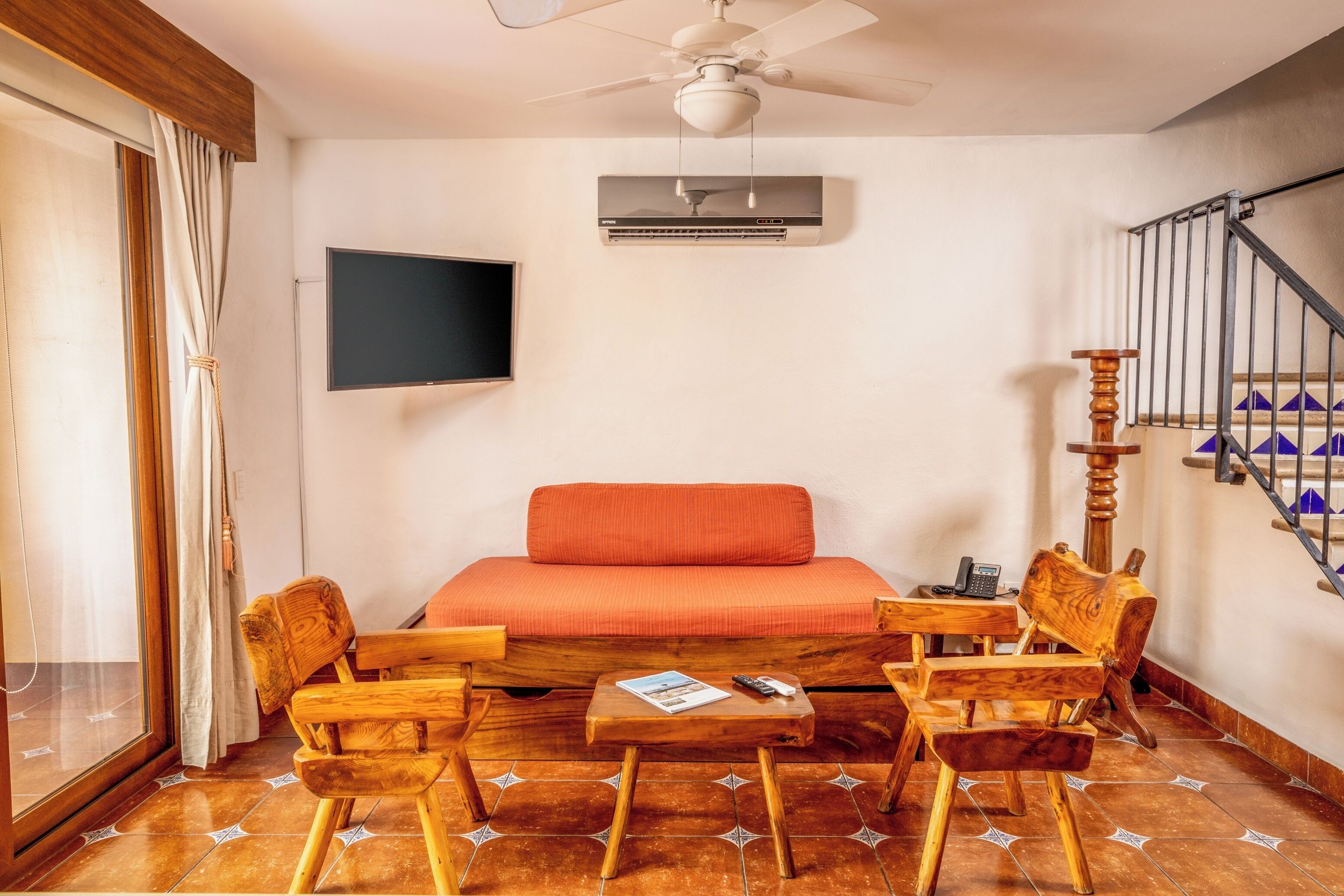 Una habitación con cama, televisión, aire acondicionado, una mesa de madera y una escalera.