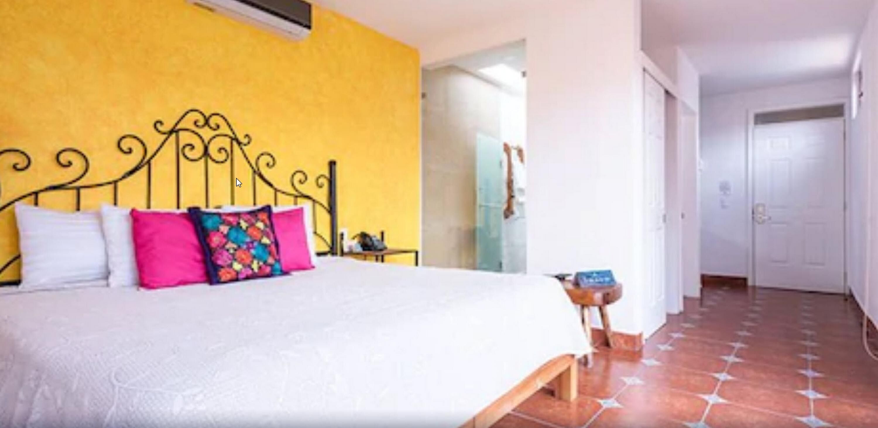 Um quarto com uma cama, parede amarela e chão de azulejos.