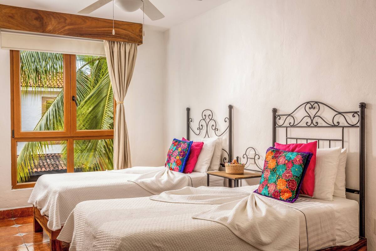 Une chambre avec deux lits, une fenêtre avec des rideaux et une vue sur des palmiers.