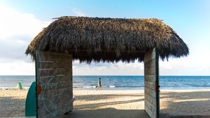 Una cabaña en la playa con techo de paja, una playa arenosa y el océano al fondo.