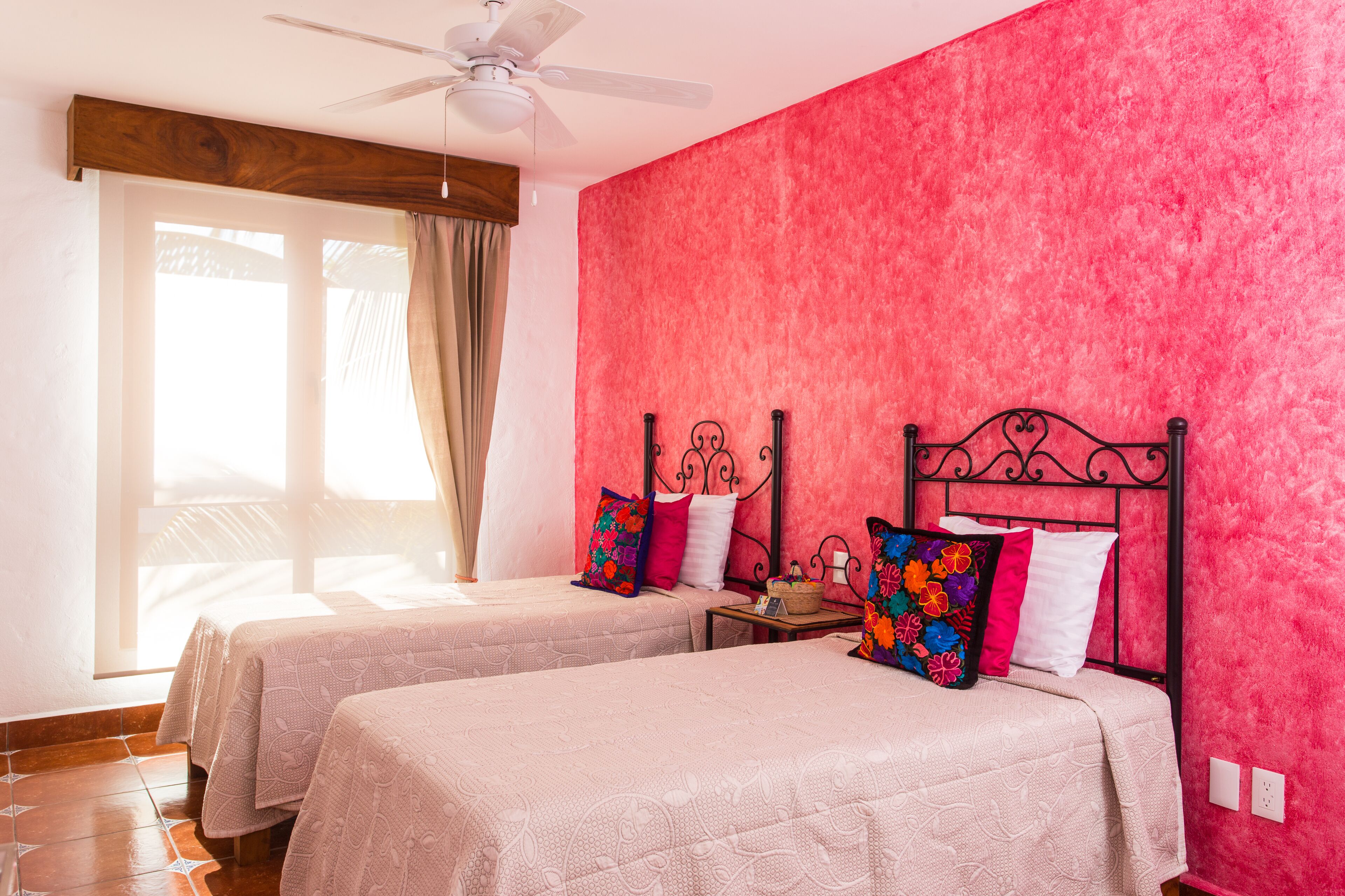 A room with two beds, a ceiling fan, and a window with curtains.