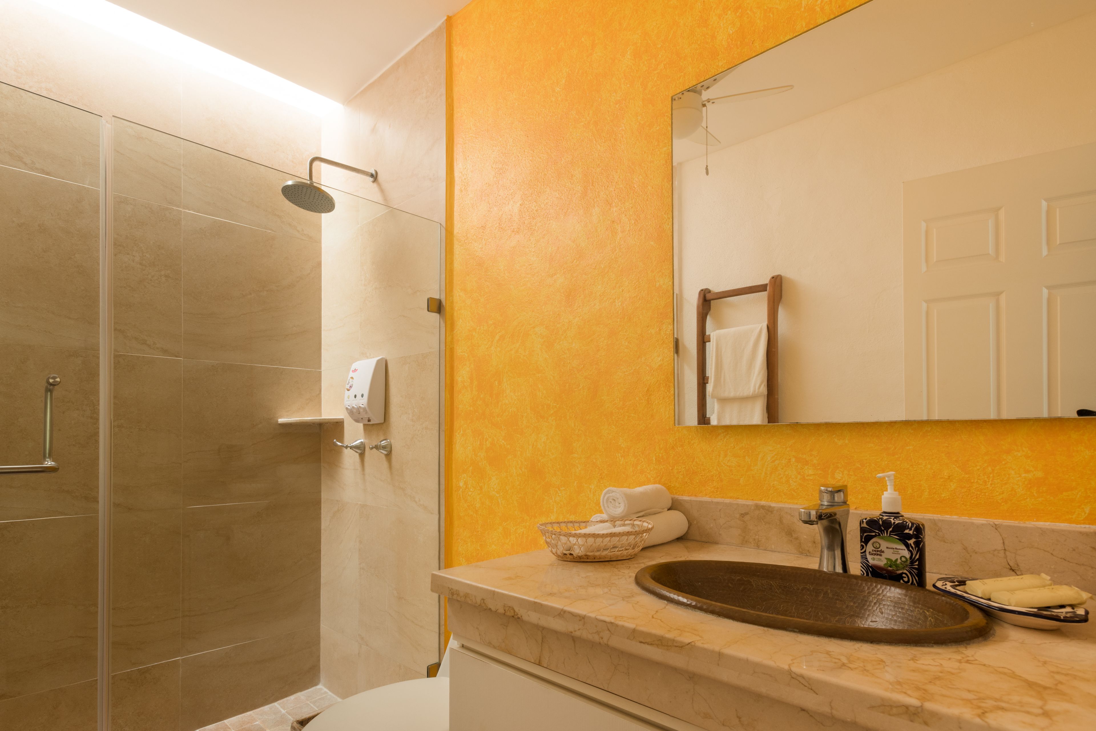 Un baño con cabina de ducha de vidrio, lavamanos de mármol y una pared de acento amarilla.