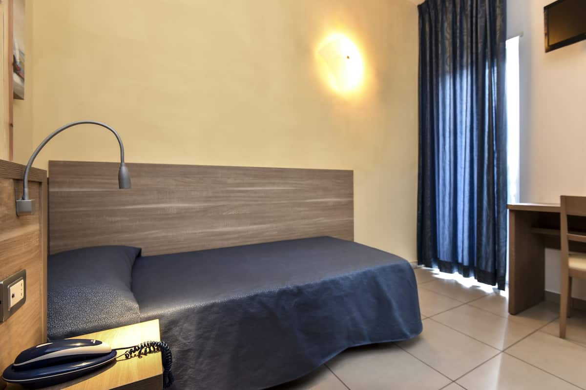 Een hotelkamer met een bed, nachtkastje, lamp en een bureau met stoel.