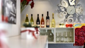 Una vitrina con botellas y copas sobre una estantería, un reloj con números y una flor roja.