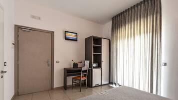 A bedroom with a bed, a desk with a chair, a wardrobe, and a window with curtains.