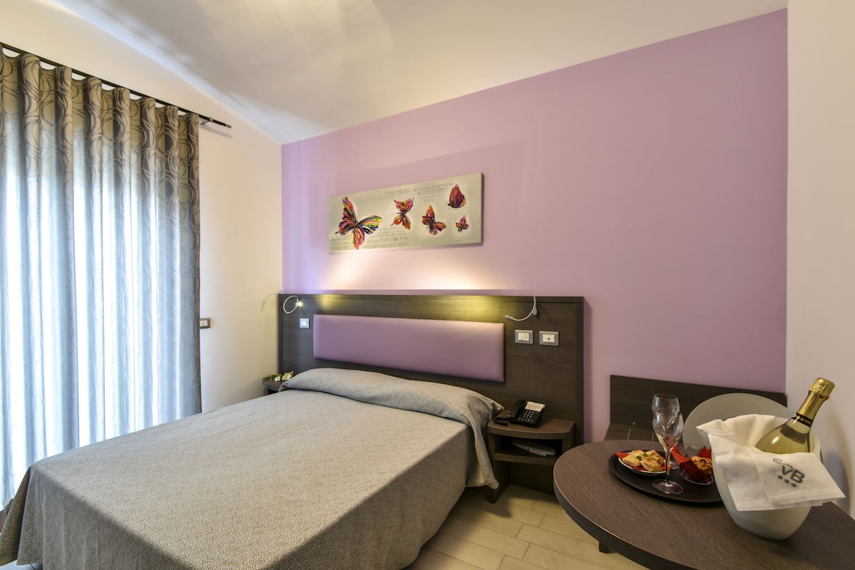 Een hotelkamer met een bed, nachtkastje en een tafeltje met een fles en glazen.