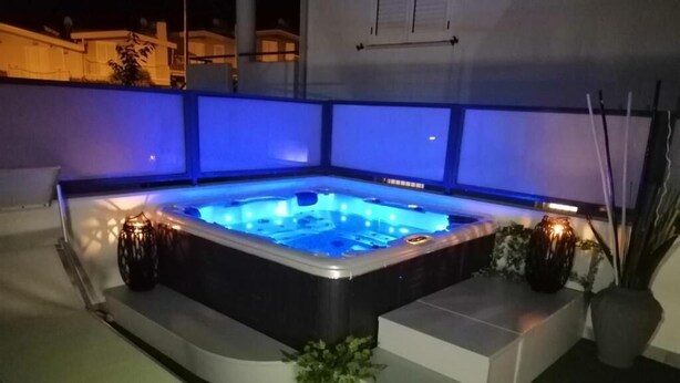 Un jacuzzi con iluminación azul, rodeado de escalones y plantas en macetas.