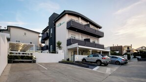 Un edificio moderno con techo plano, entrada cubierta y un área de estacionamiento con dos autos.
