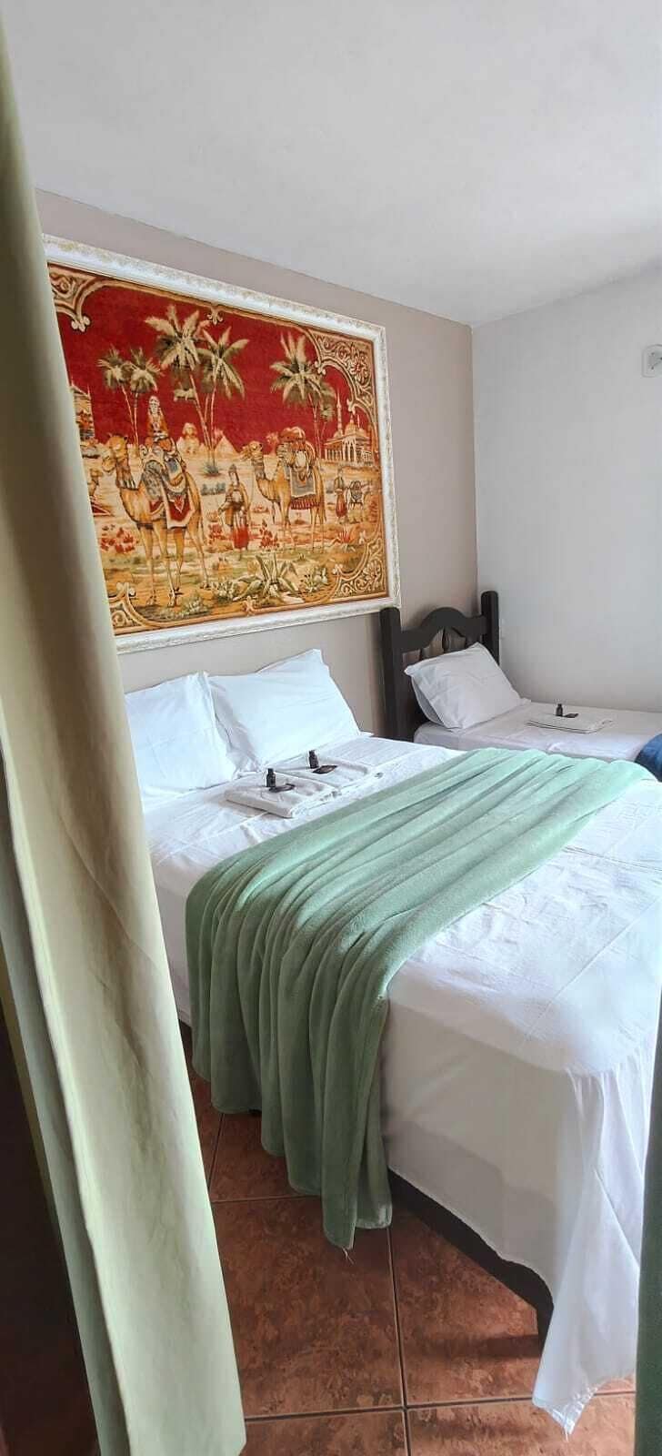 A hotel room with two beds, a large tapestry on the wall, and a tiled floor.