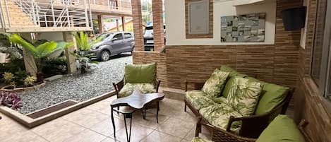 A covered outdoor seating area with a wicker sofa and chairs, a small table, and a tiled floor.