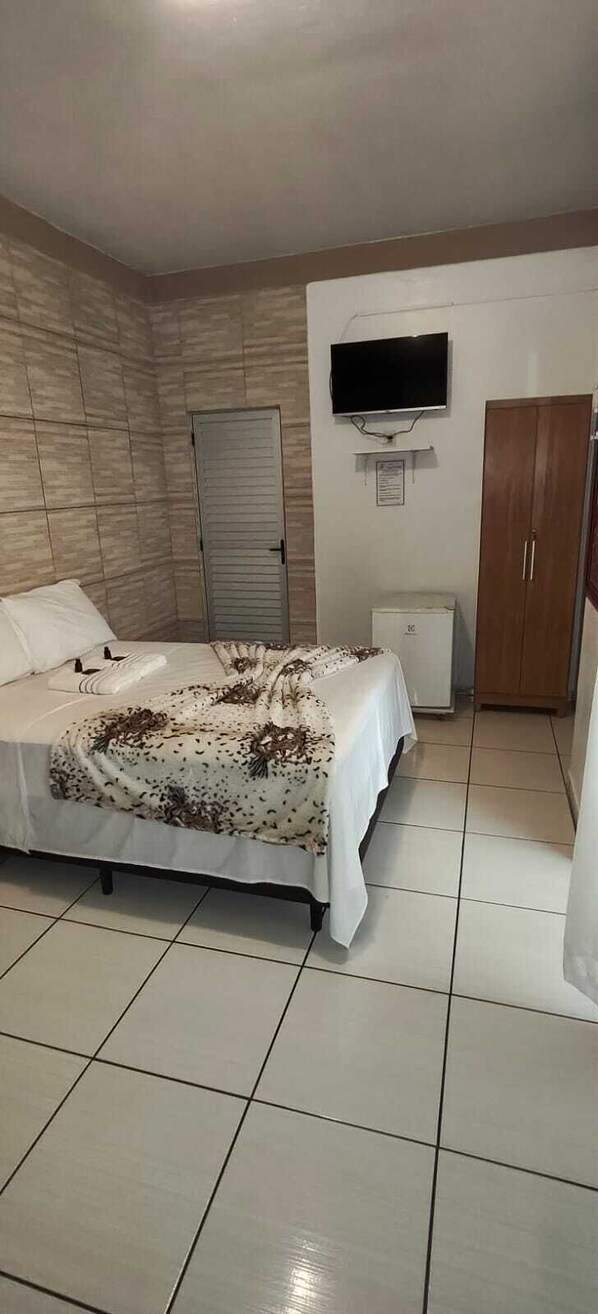 Une chambre à coucher comprenant un lit, un téléviseur fixé au mur, une armoire et un petit appareil électroménager blanc.