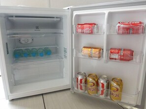 Un refrigerador abierto con estantes que contienen botellas de agua, latas de Coca-Cola y latas de SKOL.
