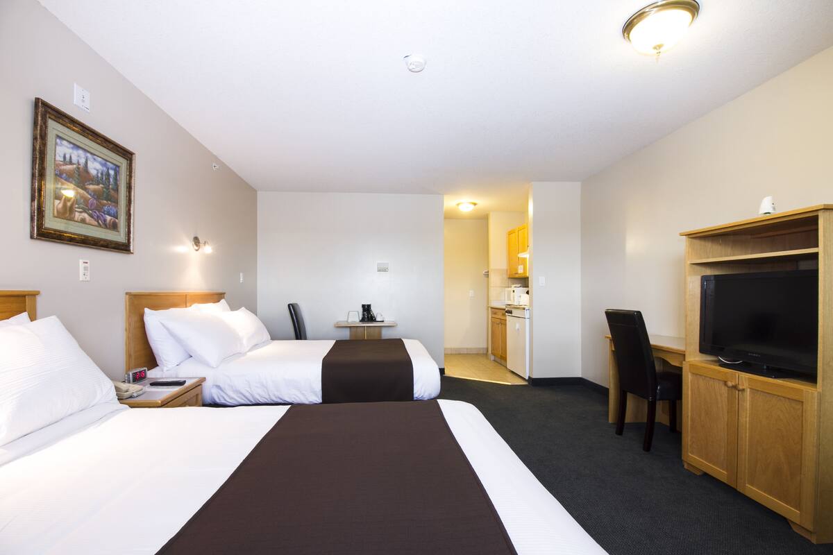 A hotel room with two beds, a desk with a chair, a television, and a kitchenette.