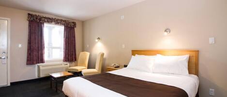 Quarto de hotel com uma cama grande, duas cadeiras, uma escrivaninha e uma janela com cortinas.