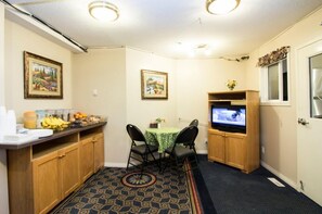 A small kitchen area with a dining table, chairs, a television, and a cabinet. - West Country Inn (Drayton Valley)