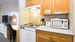 A compact kitchenette with wooden cabinets, a microwave, a toaster, and a small stove. - West Country Inn (Drayton Valley)