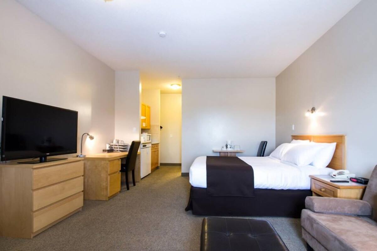 A hotel room with a bed, a desk, a television, a chair, a couch, and a small kitchenette.