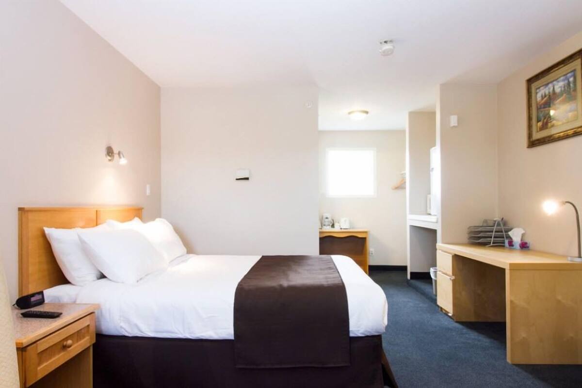 A hotel room with a bed, bedside table, desk, and chair.