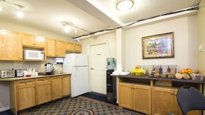 A compact kitchen with wooden cabinets, a microwave, a refrigerator, and a water dispenser. - West Country Inn (Drayton Valley)