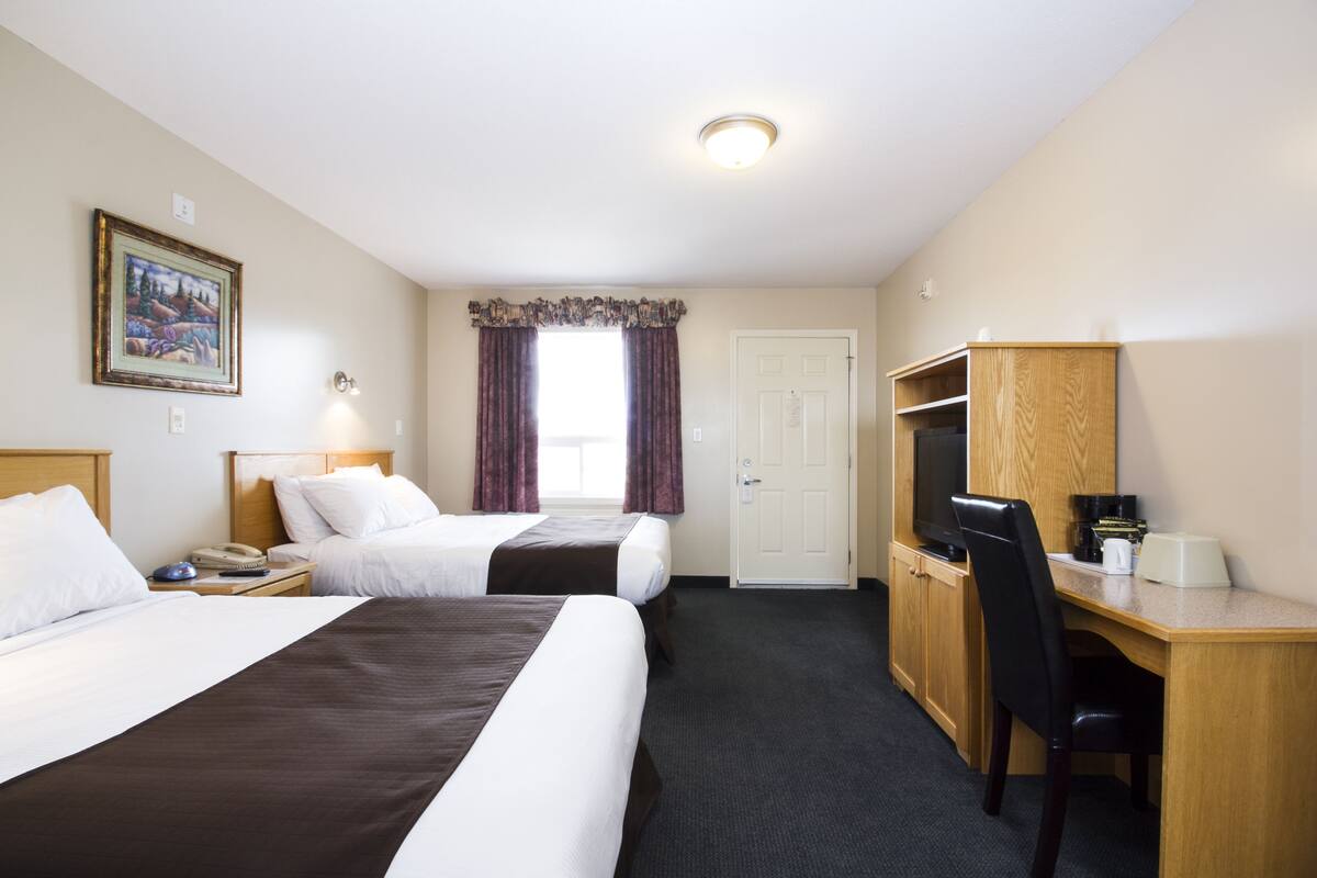 A hotel room with two beds, a desk, a chair, a television, and a door.