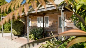 A wooden cabin with a porch, surrounded by greenery and a clear sky. - Abel Tasman Lodge (Marahau)
