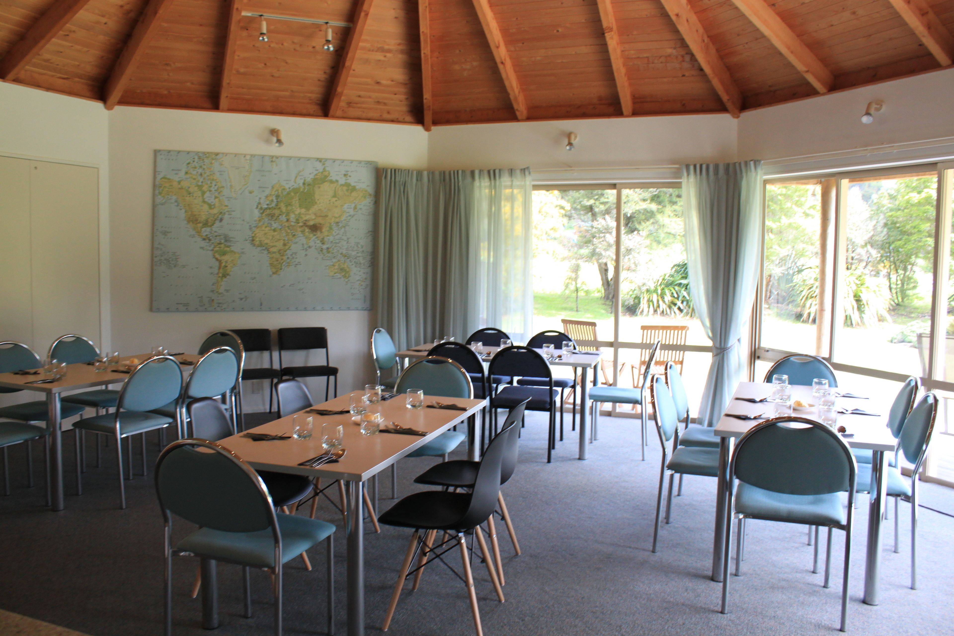 A conference room with tables and chairs, a large world map on the wall, and large windows with curtains.