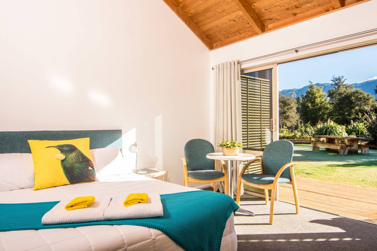 A hotel room with a bed, two chairs, a small table, and a view of the outdoors.