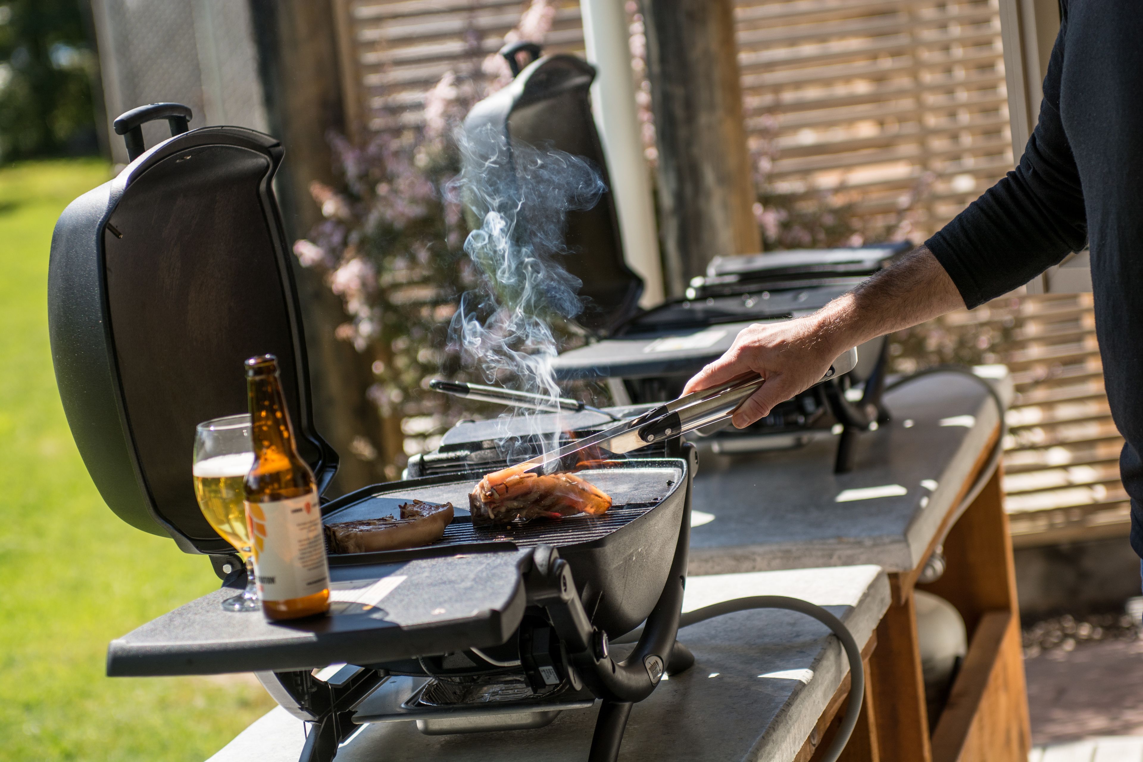 A portable grill with a bottle of beer and a glass on a table.