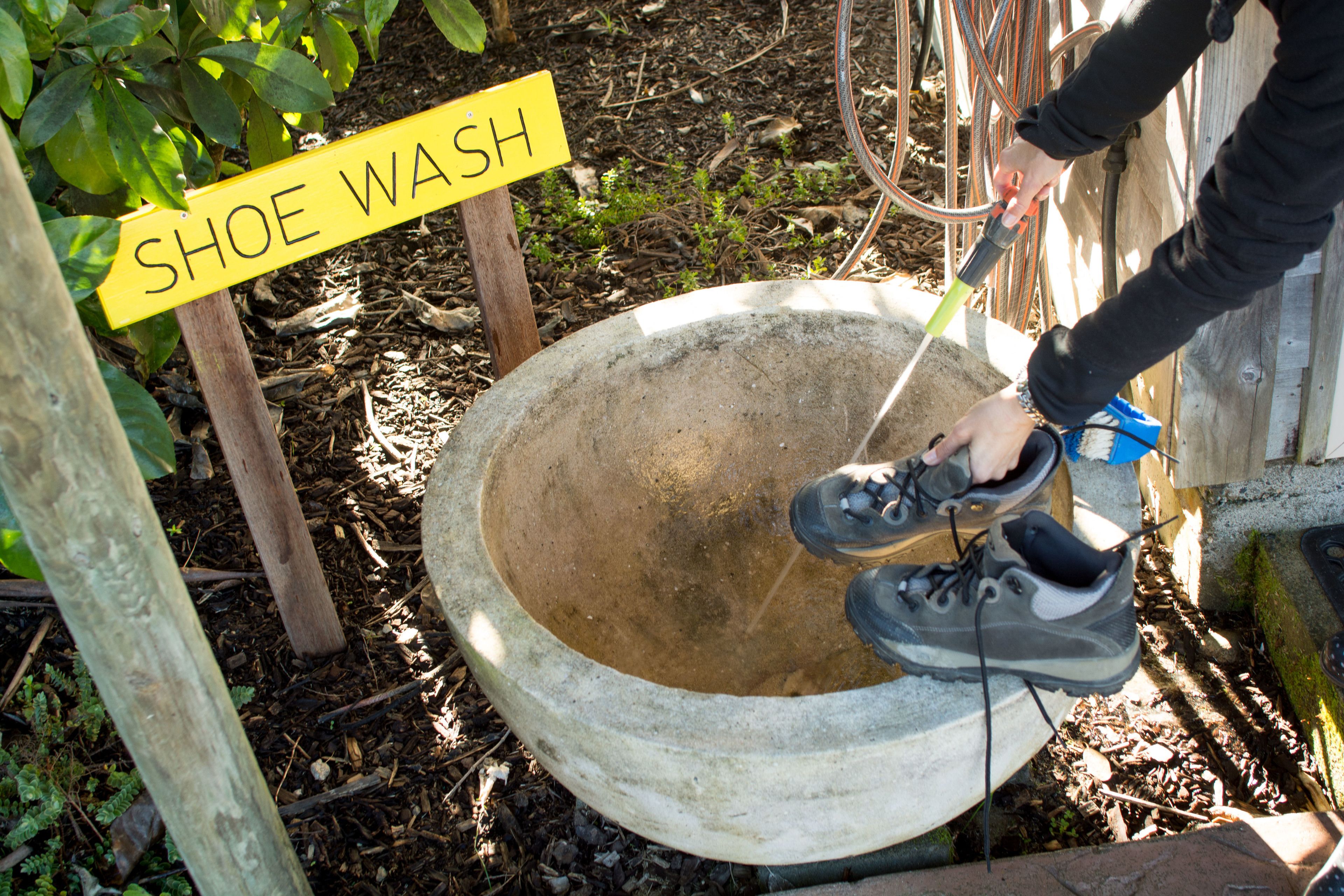 Eine Person wäscht Schuhe in einem Betonbecken, mit einem Schild, auf dem 'SHOE WASH' steht.