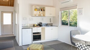 A modern kitchen with white cabinets, a built-in oven, and a window with a view of greenery. - Abel Tasman Lodge (Marahau)