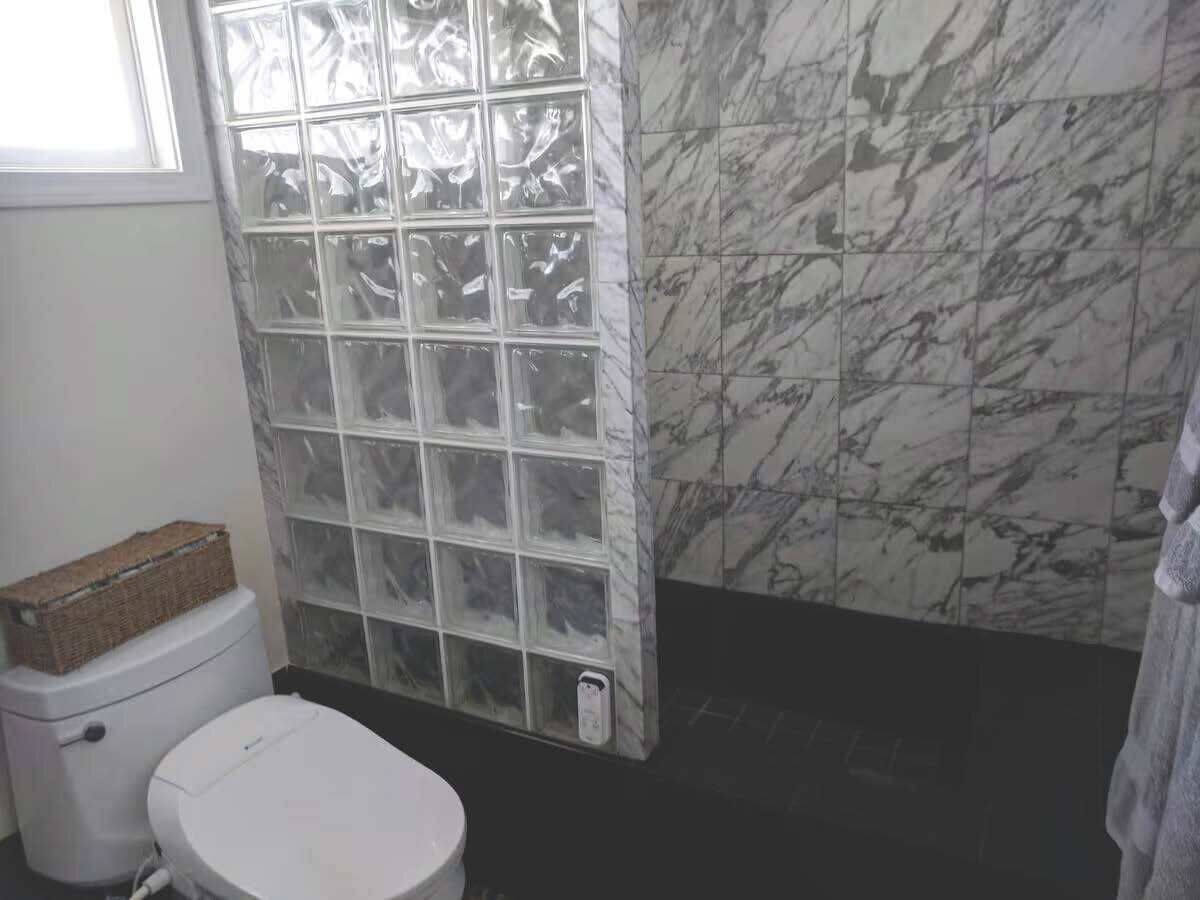 A bathroom with a toilet, a glass shower enclosure, and marble walls.