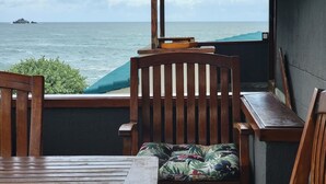 Un banco de madera con un cojín floral, una mesa de madera y vista al océano a través de una ventana.