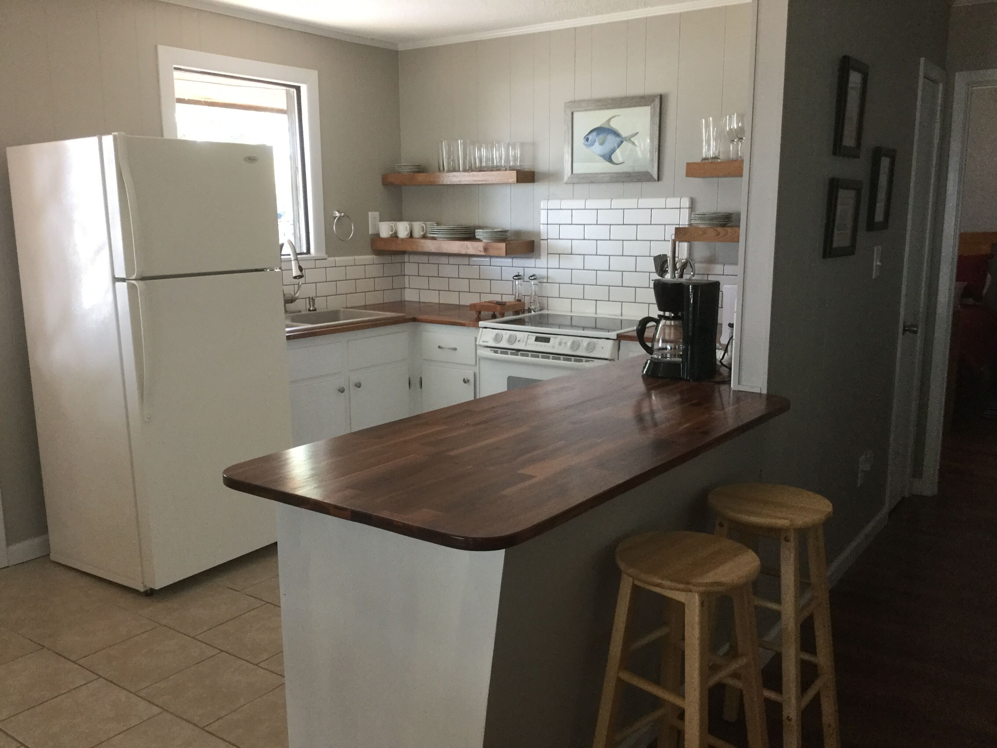 Eine Küche mit weißen Schränken, einem weißen Kühlschrank, einer Holz Arbeitsplatte, einer Kaffeemaschine und zwei Barhocker.