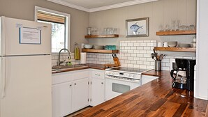 Cocina con armarios blancos, un lavamanos de acero inoxidable, una estufa y repisas de madera sobre la encimera.