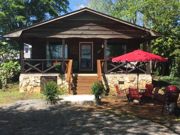 A rustic cabin with a stone foundation, a wooden porch, and a red umbrella.