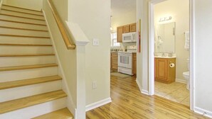 A staircase with wooden steps and white walls, leading to a kitchen with wooden cabinets, a microwave, and a stove. - Comfortable and Clean Townhouse, One Block From beach (Myrtle Beach)