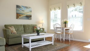 A living room with a green sofa, a white coffee table, and a dining area with white chairs and a table. - Comfortable and Clean Townhouse, One Block From beach (Myrtle Beach)