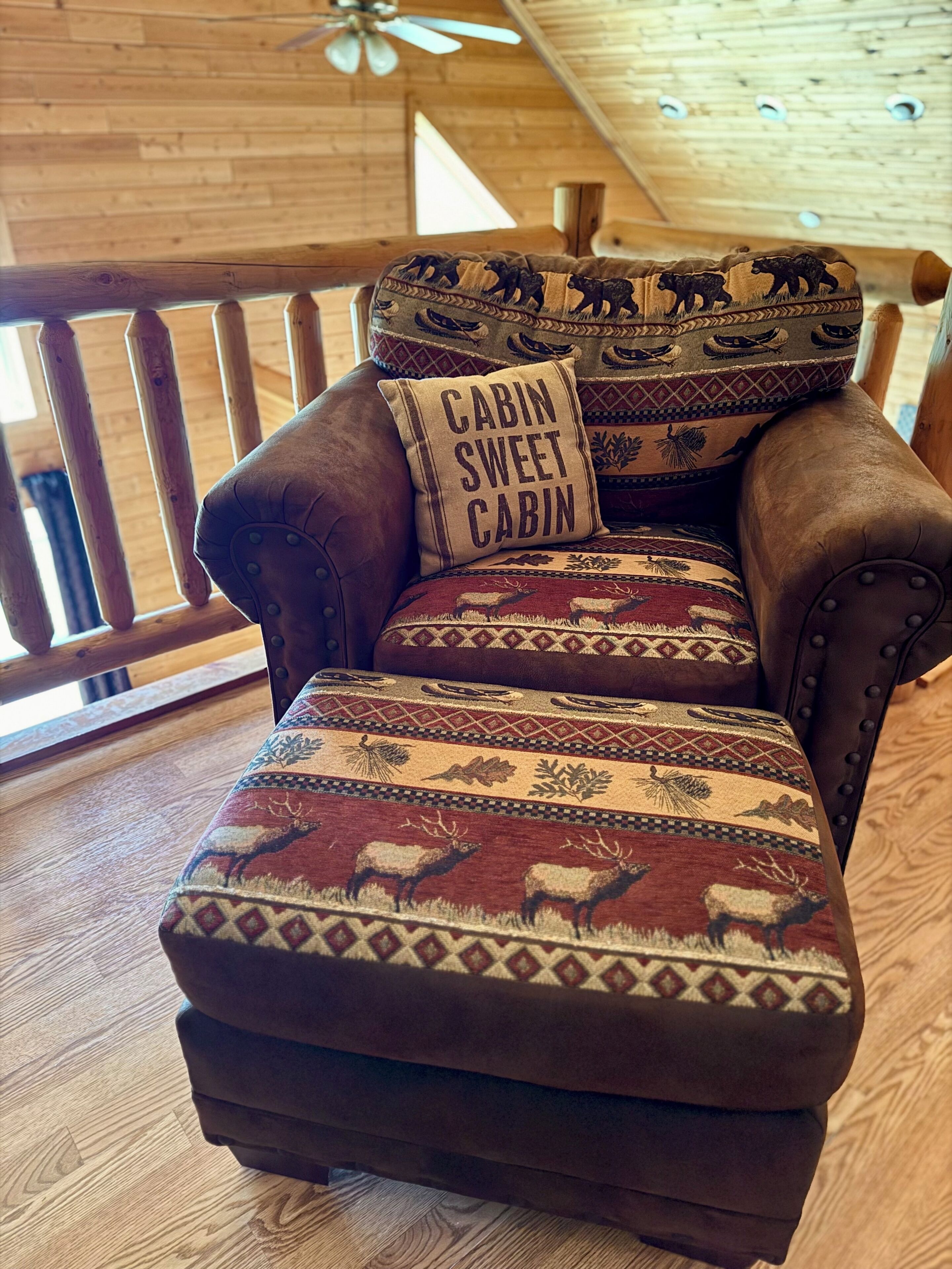 A wooden cabin interior with a leather couch, patterned cushions, and a 'Cabin Sweet Cabin' pillow.